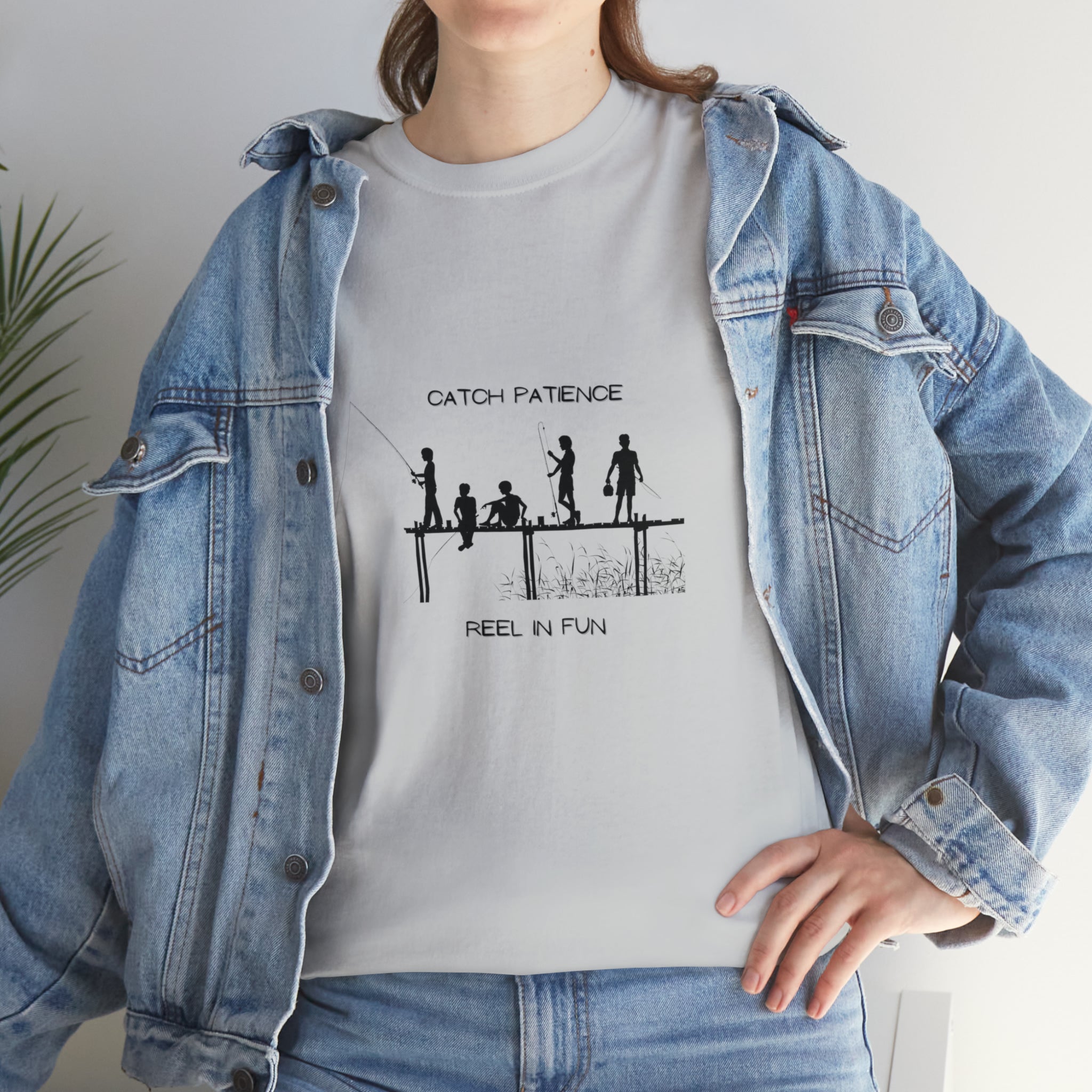 Front view of Adult female wearing white T-shirt with "Catch Patience Reel in Fun" inspired graphic of people fishing with jean jacket.