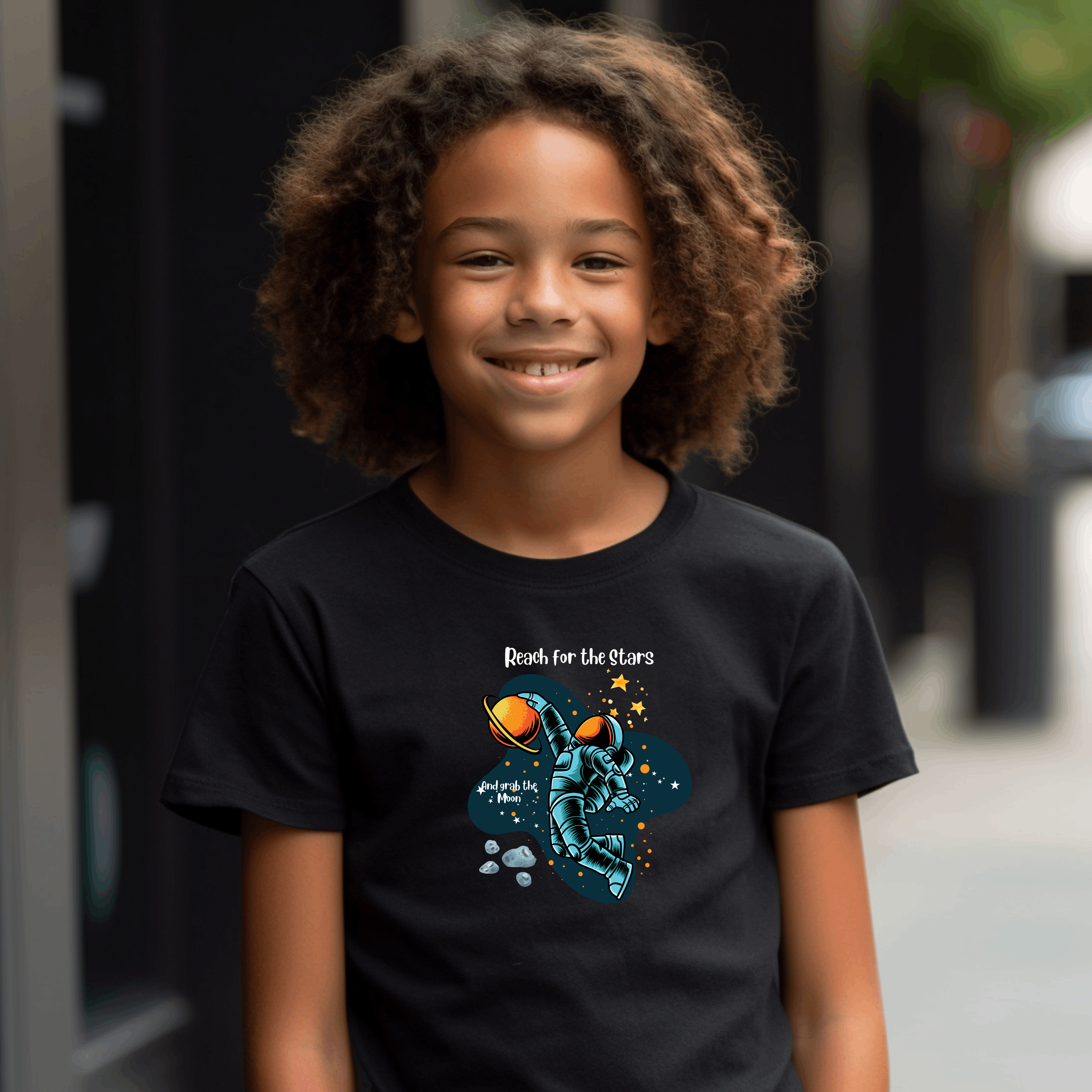 Youth Boy wearing unisex black T-Shirt with "Reach for the stars but grab the moon" motivational image on front.