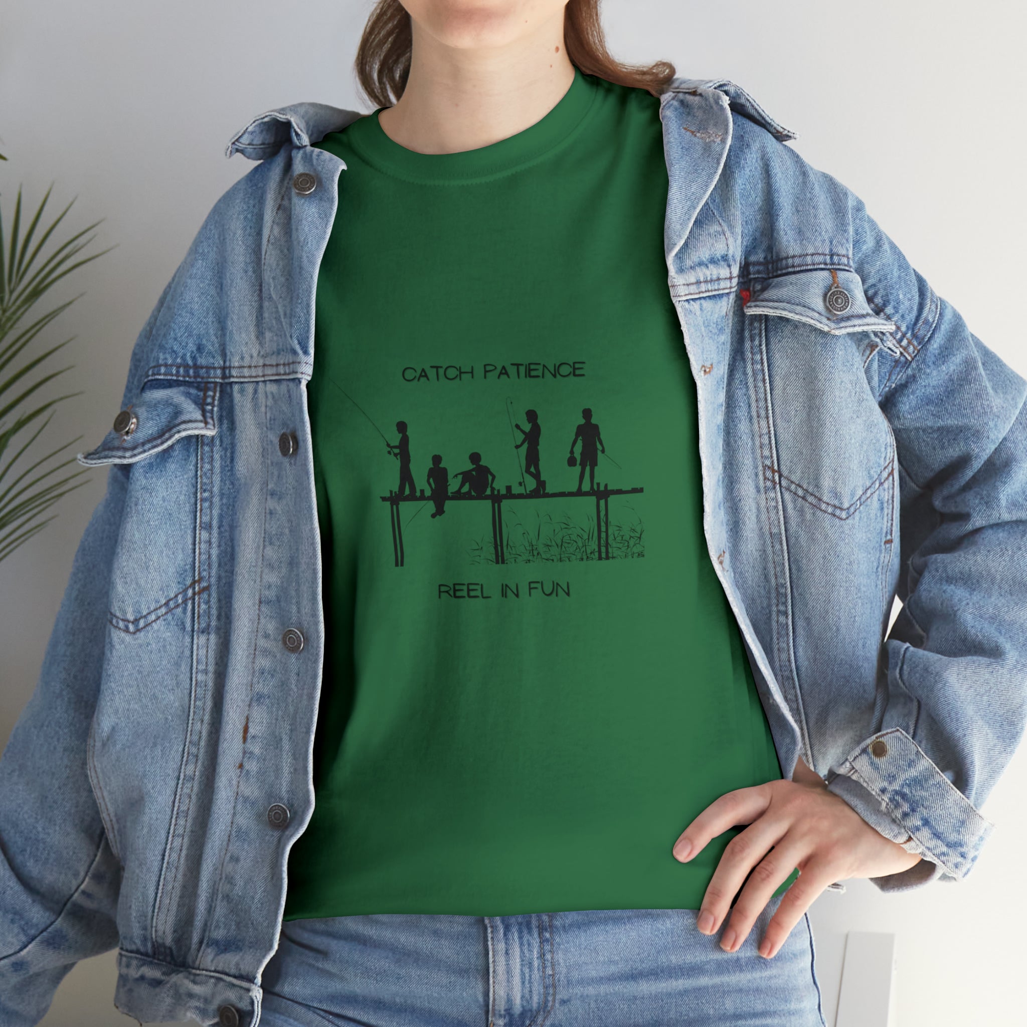 Front view of Adult female wearing irish green  T-shirt with "Catch Patience Reel in Fun" inspired graphic of people fishing with jean jacket.