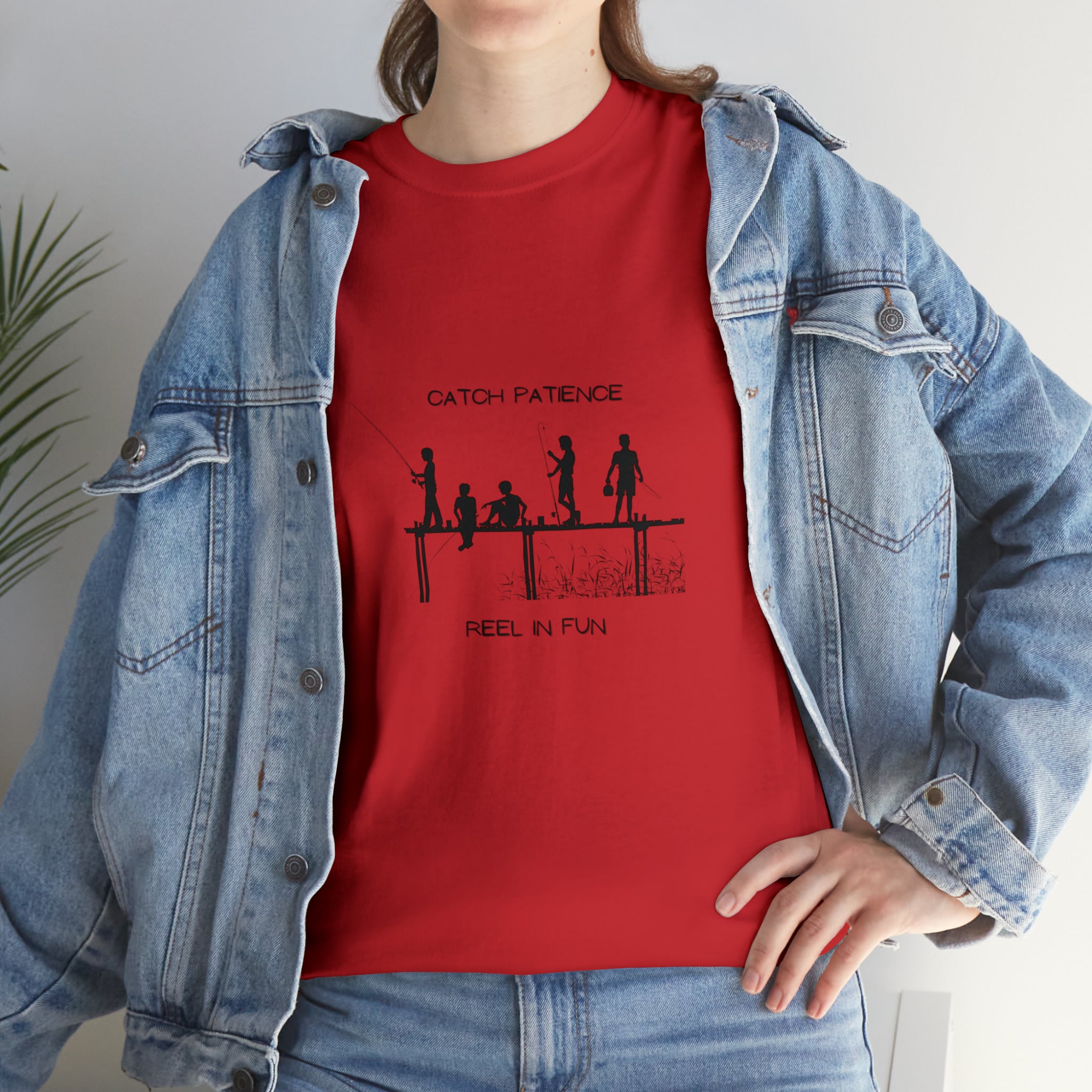Front view of Adult female wearing red T-shirt with "Catch Patience Reel in Fun" inspired graphic of people fishing with jean jacket.