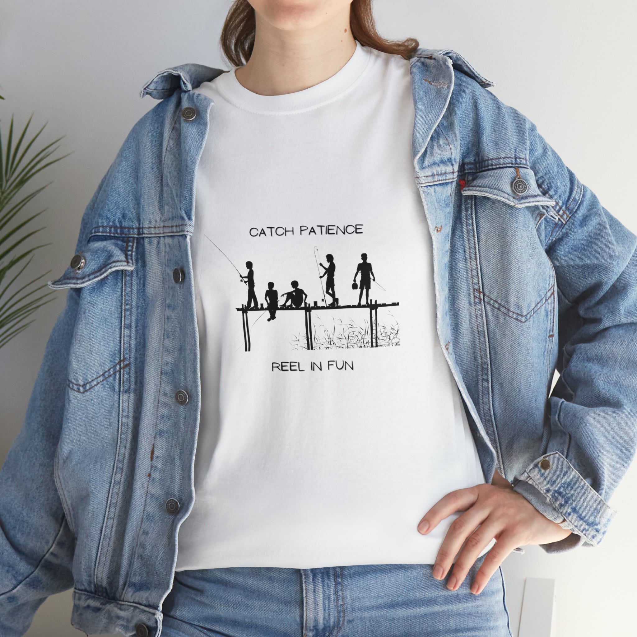 Front view of Adult female wearing white T-shirt with "Catch Patience Reel in Fun" inspired graphic of people fishing with jean jacket.