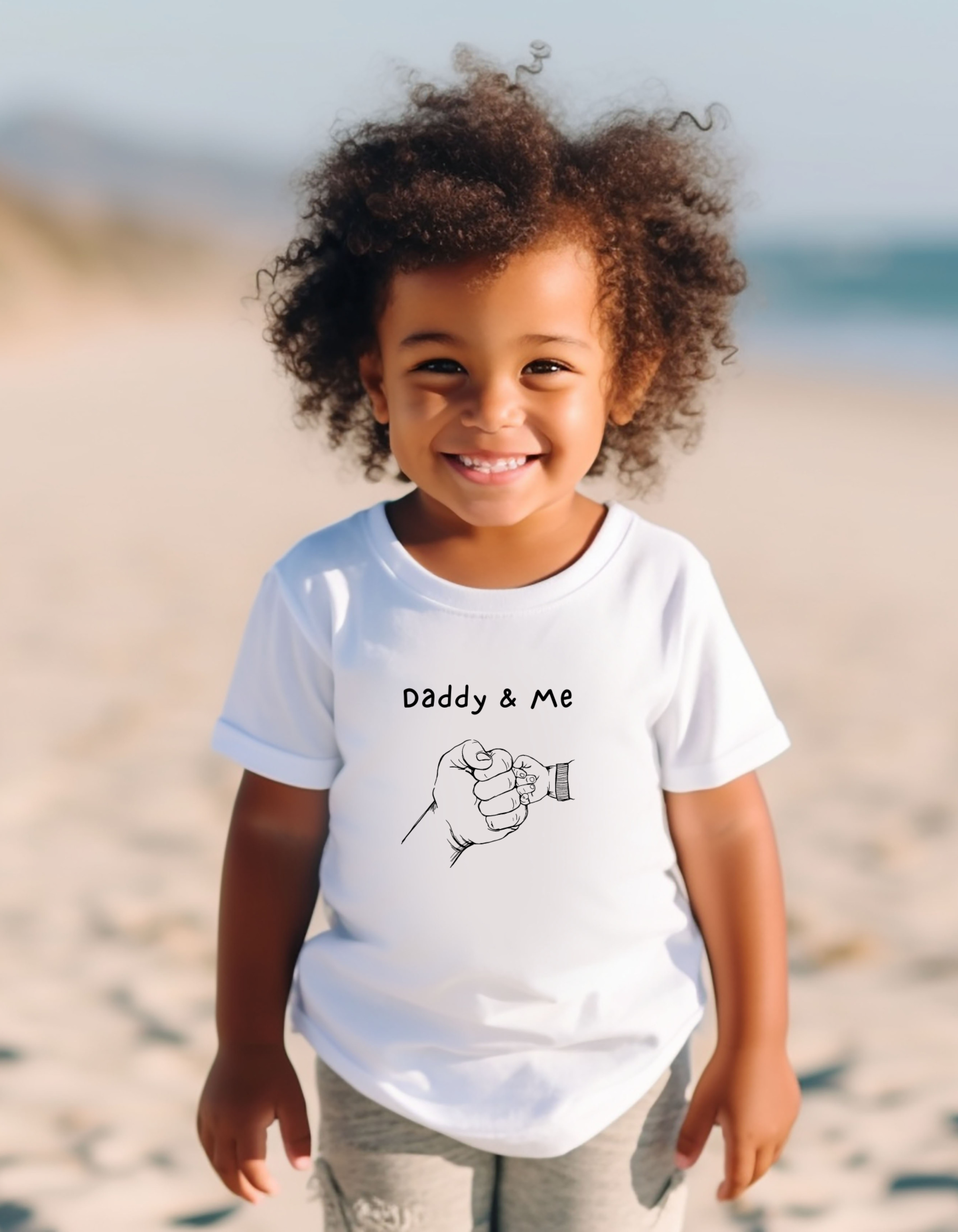 Toddler Boy wearing white unisex T-Shirt with "Daddy & Me" inspired fist bump graphic on front.